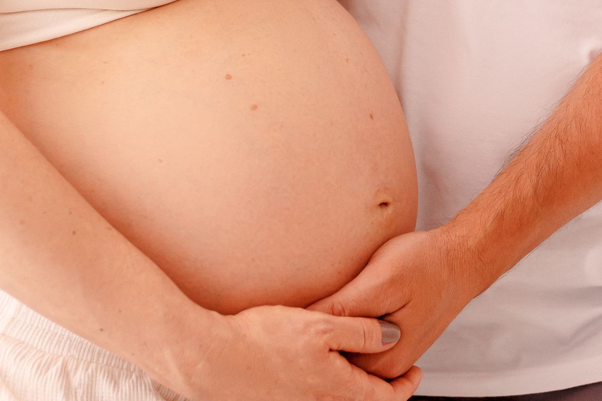 Barriga de gestante com as mãos do casal entrelaçadas