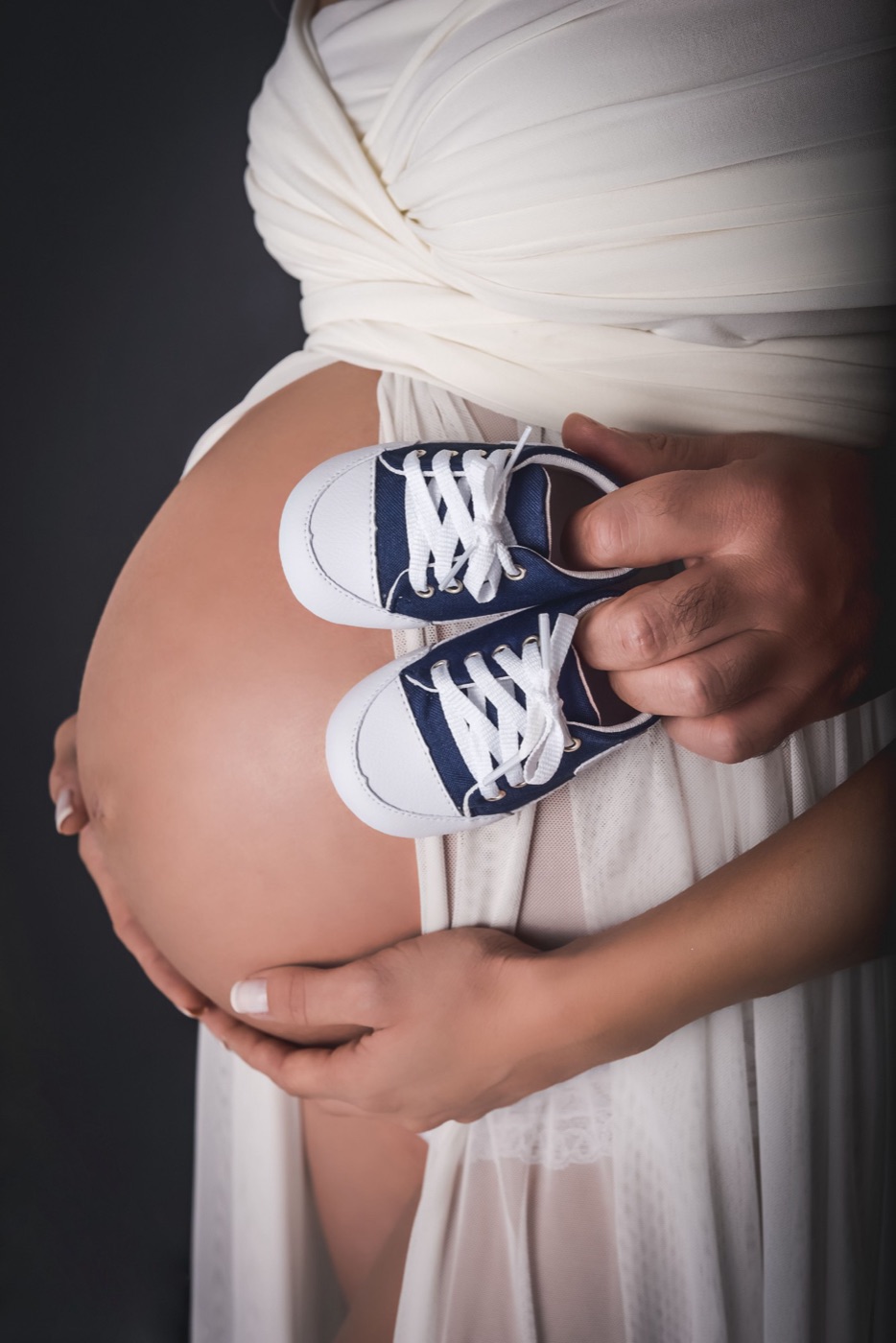 Barriga de gestante com um par de tênis de bebê nas mãos do casal